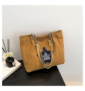 Detail of mustard yellow suede tote bag featuring a denim star patch and metal chain strap
