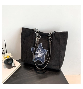 Detail of black faux suede tote bag featuring a denim star patch and metal chain strap