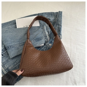 Détail du sac hobo avec motif tissé en losanges marron sur fond en jean et livre d'art