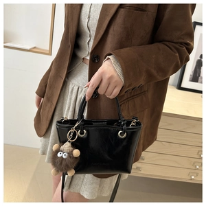 Detail of glossy black bucket bag with brown cartoon fur ball charm and embossed text