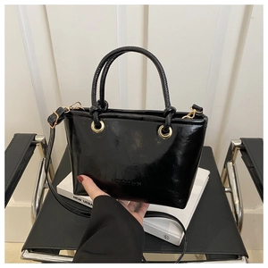 Detail of black patent leather bucket bag with gold hardware and removable shoulder strap