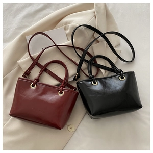 Detail of burgundy and black glossy faux leather mini tote bags on a beige blazer