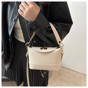 Close-up of beige lychee texture small square bag with gold twist-lock on black jacket