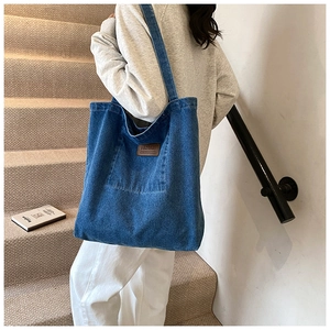 Detail of blue denim tote bag with brown leather brand patch and functional front pocket