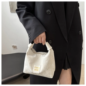 Detail of cream pleated fabric shoulder bag styled with a minimalist black coat look