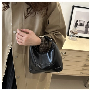Detail of black patent leather underarm bag with letter embossing and half-moon curve