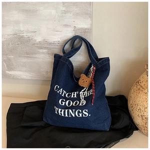 Close-up of denim tote bag with white text slogan and cute plush bear accessory
