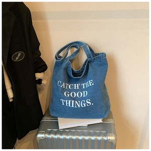 Detail of blue denim tote bag with white lettering on metallic suitcase and book