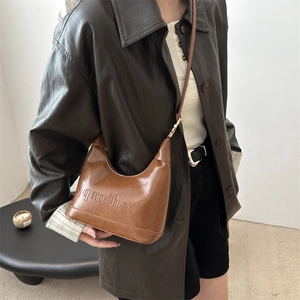 Brown vintage faux leather baguette bag with letter engraving held by a model in brown leather jacket