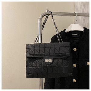Detail of black quilted shoulder bag featuring metal chain strap and rectangular turn-lock