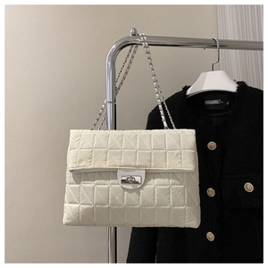 Close-up of beige quilted chain bag featuring a silver twist lock and woven strap