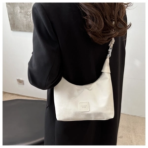 Macro detail of white pleated crescent bag featuring polished finish and FASHION BAGS tag