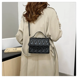 Détail du sac matelassé noir avec chaîne épaisse et texture géométrique en 3D