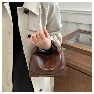 Close-up of the embossed micashe logo on a dark brown polished faux leather tote bag