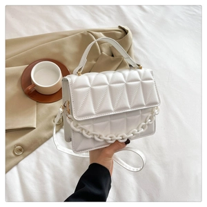 Détail d'un sac à bandoulière blanc matelassé avec chaîne acrylique et finitions dorées
