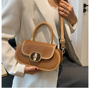 Borsa a tracolla in pelle marrone con fibbia dorata indossata su un blazer bianco