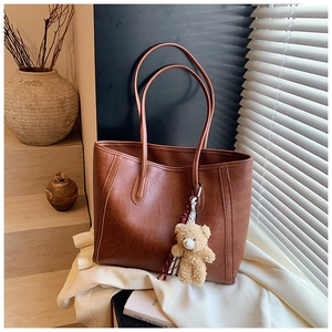 Detail of dark brown leather tote bag with vintage texture and plush bear pendant
