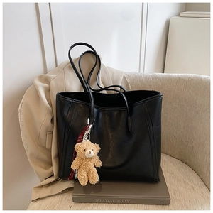 Detail of black tote bag featuring a cute plush bear charm and striped scarf decoration