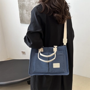 Blue canvas tote bag with front pockets and beige straps shown on a model's shoulder