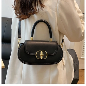 Dettaglio di una borsa a tracolla in pelle nera con fibbia dorata su un abito beige