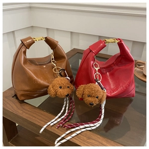 Close-up of hobo tote bags with embossed logo and cute teddy dog charms on a table