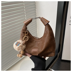 Detail of a brown pleated half-moon bag featuring a vintage texture and cute plush sheep charm