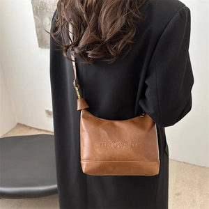 Brown textured leather tote bag with embossed logo worn on shoulder over black coat