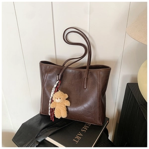 Detail of dark brown leather tote bag texture with a cute plush bear pendant accessory