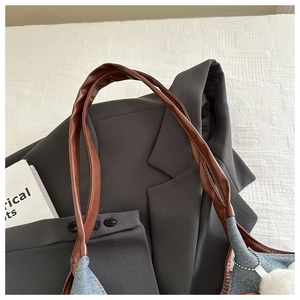 Dettaglio borsa tote in denim blu con manici in finta pelle marrone e ciondolo in peluche bianco