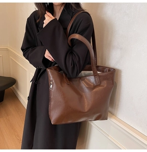 Close-up of a large brown leather tote bag showing fine texture and side zipper detail