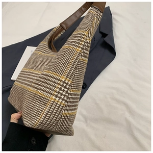 Detail of vintage plaid tote bag featuring brown leather strap on fabric texture