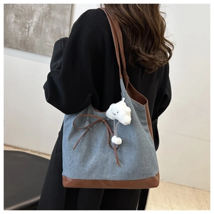Dettaglio della borsa tote in denim con tracolla in pelle, fiocco e ciondolo peluche