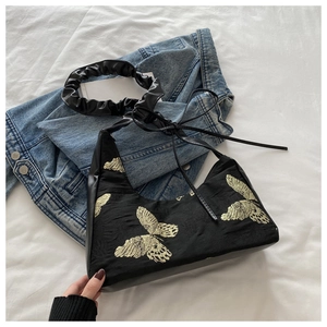 Dettaglio del ricamo a farfalla dorata su raso nero con manico a pieghe scrunchie