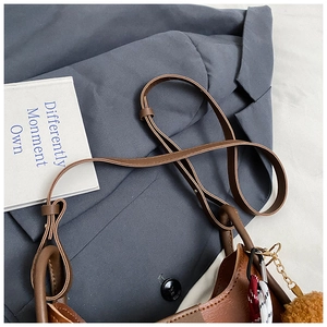 Detail of a brown leather shoulder bag with a plush pompom and woven strap decoration