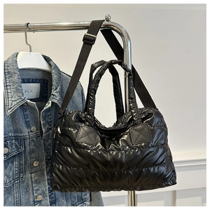 Close-up of black glossy quilted pillow tote bag with adjustable strap and square stitching