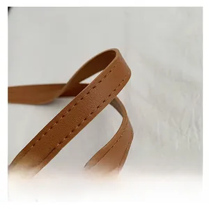 Detailed macro view showing the reinforced brown leather handle and stitching of the tote bag