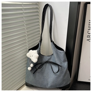 Dettaglio della borsa tote in denim con manici in pelle, fiocco nero e ciondolo a nuvola