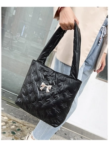 Detail of black quilted tote bag featuring bow patterns and silver metal bow accessory