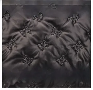 Detailed macro view of black satin tote bag with quilted 3D bow pattern and premium texture