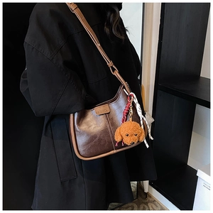 Close-up of retro brown shoulder bag with oiled leather finish and teddy bear charm