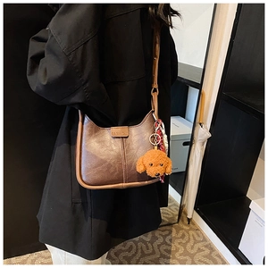 Detail of dark brown vintage leather shoulder bag with cute teddy bear plush charm