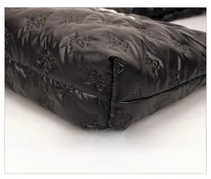 Detailed close-up of black quilted tote bag with bow embroidery and shiny nylon texture