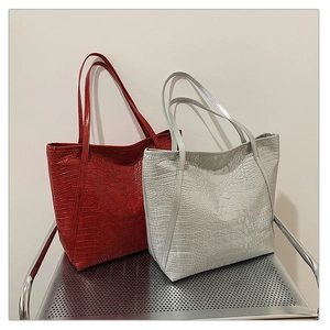 Detailed comparison of red and silver crocodile pattern tote bags on a metal stand