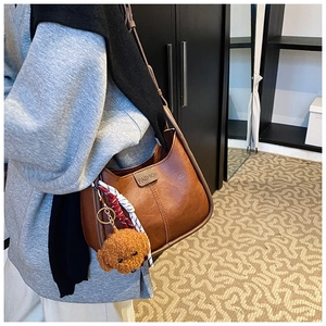 Detail of vintage brown hobo bag with teddy bear charm and silk scarf on the strap