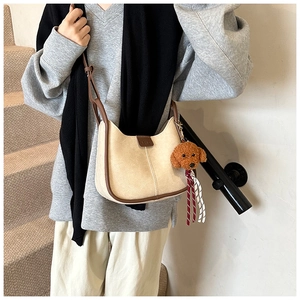Detail of a beige crossbody bag with brown trim and cute teddy bear charm accessory
