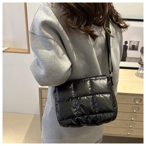 Close-up of black glossy quilted crossbody bag featuring adjustable strap on model