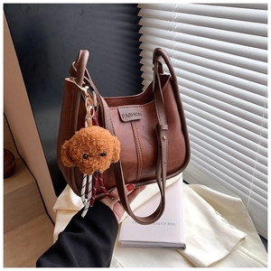 Detail of a brown leather shoulder bag with FASHION label and plush teddy bear charm