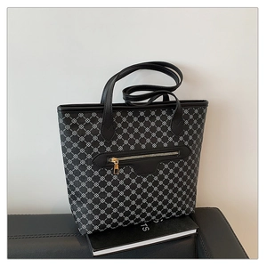 Detail of printed tote bag with interlocking logo pattern on leather sofa with books