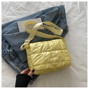 Close-up of quilted yellow crossbody bag with adjustable strap on white bedding scene