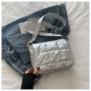 Detail of silver quilted crossbody bag with glossy finish and wide textile strap